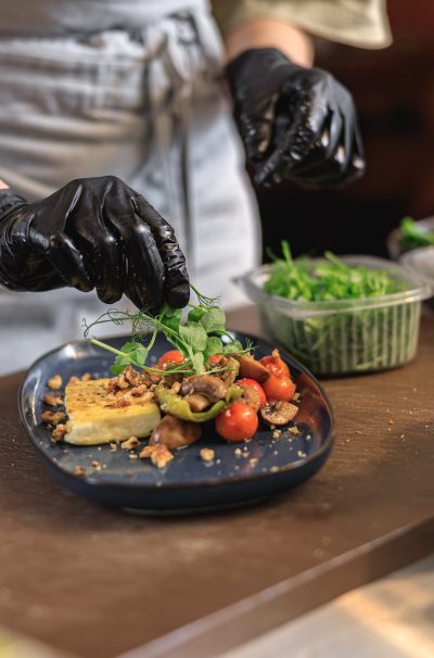 Professional chef is decorating ready meal with greens on restaurant kitchen