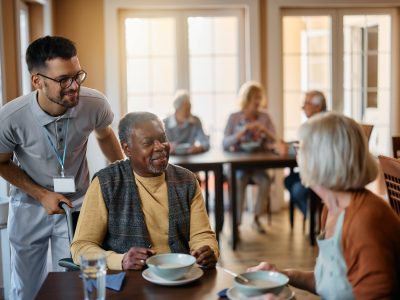 Young healthcare worker and senior people during lunch at nursing home.